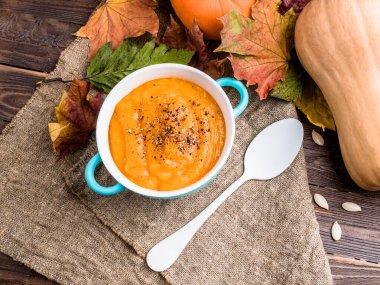 Balkabağı püresi çorbası, ahşap masa örtüsü ve sonbahar yaprakları.