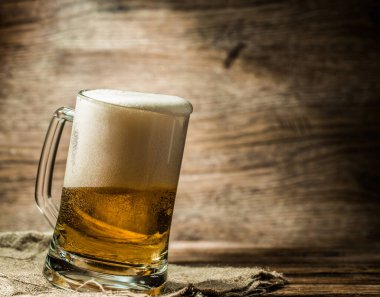 Köpüklü bira bardağa döküldü. Tahta masada duruyordu.