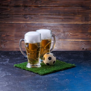 İki bardak bira, masada yeşil çimlerin üzerinde futbol topu.