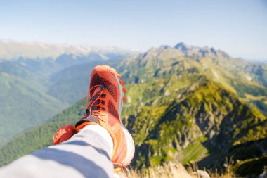 Kırmızı spor ayakkabılı ve mavi gökyüzüne karşı resim gibi dağlık manzaralı bir adam.