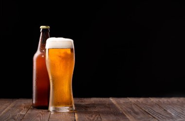 Fotoğraf: Butttle ve bir bardak bira masada ve siyah arka planda.