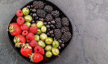 Böğürtlen, çilek, ahududu, siyah tabakta bektaşi üzümü ve boş arkaplan.