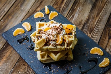Tahtada çikolata, mandalina ve dondurma bulunan birkaç Belçika waffle 'ının resmi.