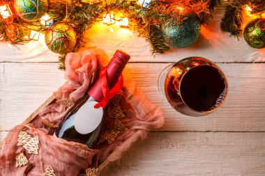 Köknar dalları, Noel baloları, yanan çelenkler, beyaz masada bir şişe şarap ve cam.