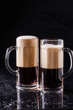 Siyah arka planda iki kupa köpüklü bira
