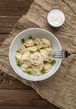 Et hamuru - Rus pelmeni, ahşap arka planda beyaz tabakta etli ravioli.