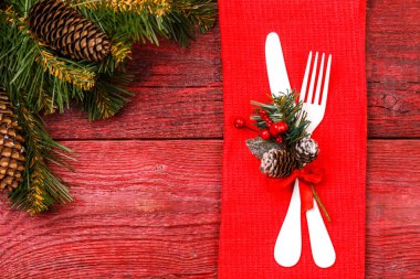 Kırmızı peçetede çatal ve bıçakla noel masasının fotoğrafı, ladin dalları, koniler.