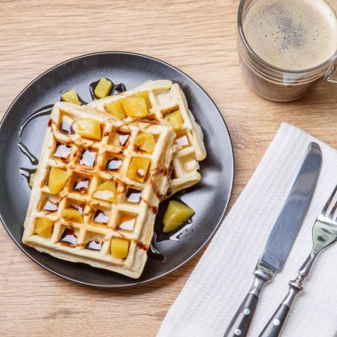 Ev yapımı waffle, mandalina, çikolata ve bir fincan kahve ve çatal bıçaklı siyah tabak.