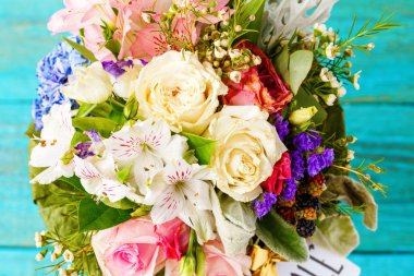 Yukarıdan fotoğrafı romantik buket pembe güller, zambaklar, ahşap mavi zemin üzerine yeşil yaprakları