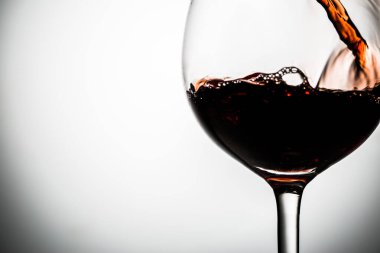 Şarap kadehinde boş arka planda kırmızı şarap dökülüyor.