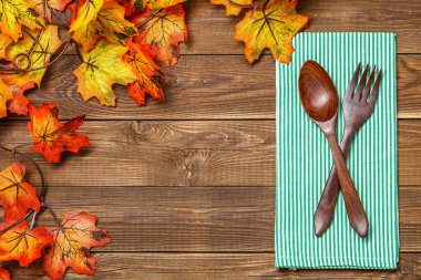 Ahşap zemin, çatal ve kaşık peçetede, akçaağaç yapraklı.