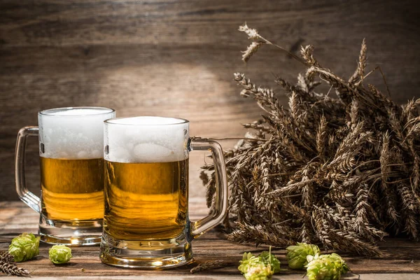 Couple of beers on table with hop and wheat in empty wooden background