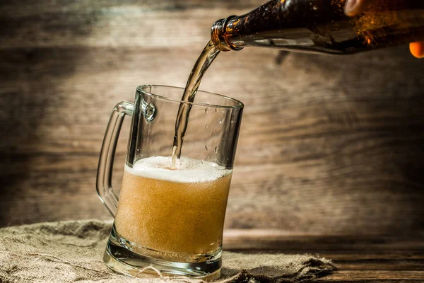 Foamy beer from bottle poured into mug standing on wooden table