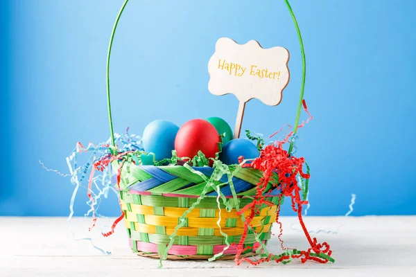 Zdjęcie Kosza Kolorowymi Jajkami Pustym Niebieskim Tle Życzeniem Szczęśliwej Wielkanocy — Zdjęcie stockowe