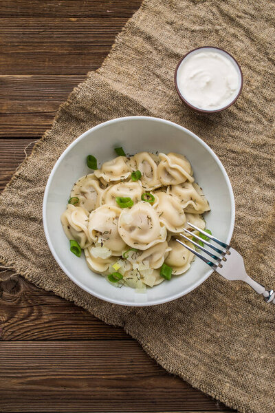 Мясные пельмени - русские пельмени, равиоли с мясом на белой тарелке на деревянном фоне
