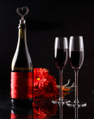 Láhev vína se zátkou ve tvaru srdce a dvě sklenice tří červených gerber. Romantický večer. Svatý Valentýn