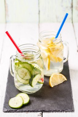 İki kupa doldurulmuş detoks ferahlatıcı su: beyaz ahşap masa üzerinde salatalık ve limon