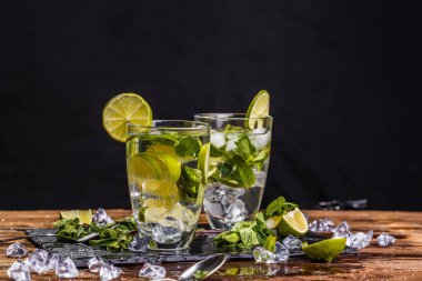 Siyah arka plandaki ahşap masada iki bardak taze mojito.