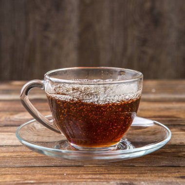 Ahşap arka plandaki masada şeffaf fincanda bitki çayı.