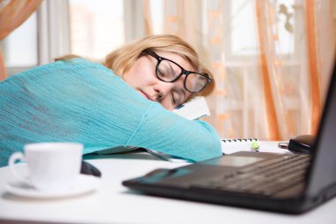 Sarışın kadın kahve ve laptopla masada uyuyor, işten sonra dinleniyor.