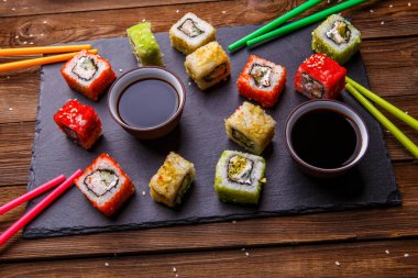 Suşi, soya soslu rulo, ahşap arka planda gri taş levhada servis edilir.