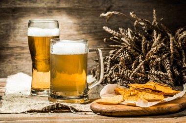 Kupa, keten kumaş üzerine bir bardak bira, buğday filizi ve patates cipsi.