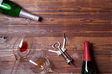 İki şişe şarap, iki şarap bardağı ve ahşap masada tirbuşon.