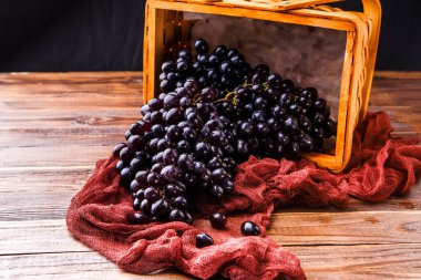 Yukarıdan görüntü: Tahta sepetteki siyah üzümler, stüdyodaki masada kırmızı bez.