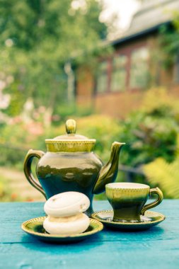 Çaydanlık ve fincanlar. Bahçedeki masada pasta var.