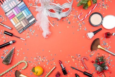 Göz gölgeleri, fırçalar, tüy maskesi, mandalina, şeker kamışı, boş kırmızı masa üzerinde konfeti, yazı için yer.