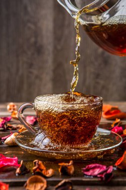 Bir sürahi çay ve kupa gül yapraklarıyla masada duruyor.