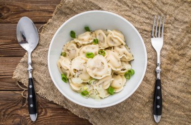 Et hamuru - Rus pelmeni, ahşap arka planda beyaz tabakta etli ravioli.