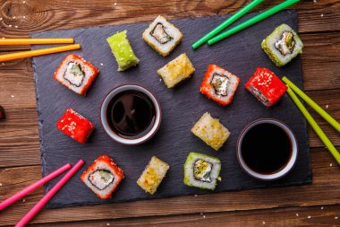 Suşi, soya soslu rulo, ahşap arka planda gri taş levhada servis edilir.
