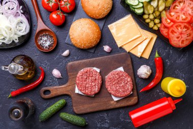 Siyah masadaki hamburgerler için malzemelerin üstüne fotoğraf.