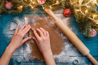 İnsan eli fotoğrafı, merdane, hamuru, ladin dalları, çelenkler, mavi masadaki bisküvi kalıpları.