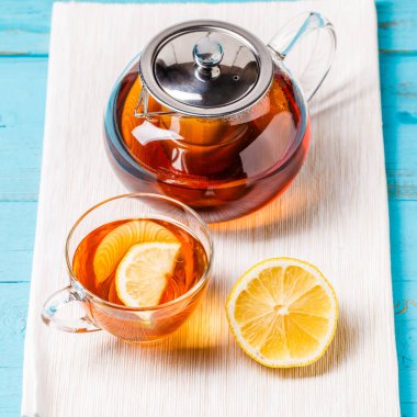 Mavi ahşap masada limonlu ve cam çaydanlıklı bir bardak çay..