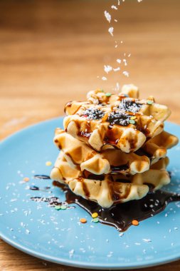 Ev yapımı waffle Çikolata ve hindistan cevizini mavi tabağa serpiyor
