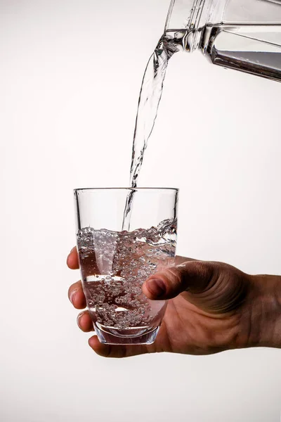 Man pours water from pitcher into glass on clean gray background