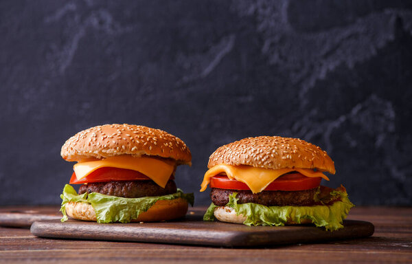 Изображение двух гамбургеров на деревянном столе на черном фоне
