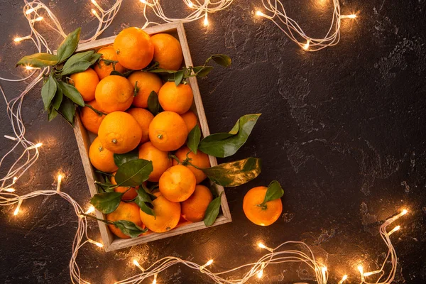 Foto Tangerinas Caixa Madeira Com Guirlanda Ardente Mesa Preta — Fotografia de Stock