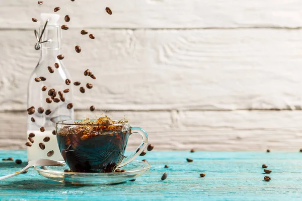 Image of a cup of coffee, a jug of milk with falling coffee beans and copyspace