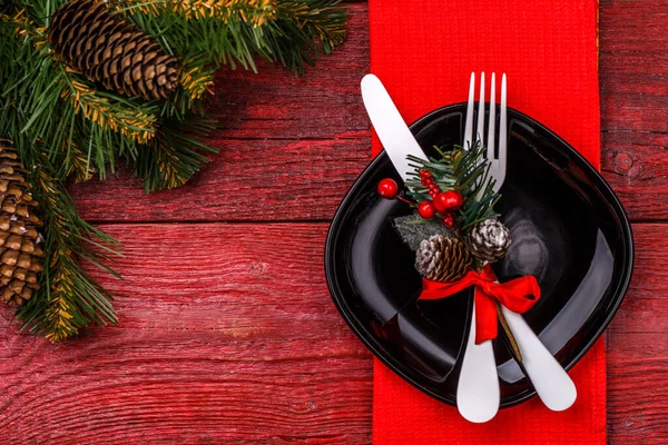 圣诞餐桌摆设为红色餐巾 黑色盘子 白色叉子和小刀 装饰过的寄生枝和圣诞松树枝条 圣诞节背景 — 图库照片