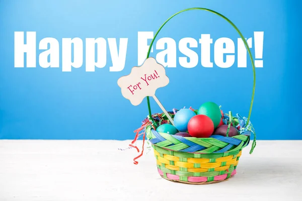Zdjęcie Kosza Kolorowymi Jajkami Pustym Niebieskim Tle Życzeniem Szczęśliwej Wielkanocy — Zdjęcie stockowe
