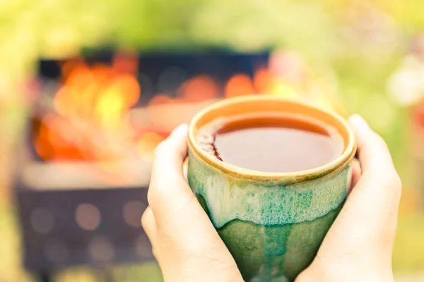 Elleri çay fincanı, brazier ve arkasında ateş tutuyordu.