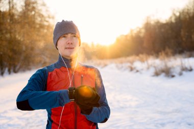 Kulaklıkla sıcak spor giysiler giyen koşucu modern akıllı saate bakıyor ve kış eğitiminde harcanan kalorileri sayıyor.