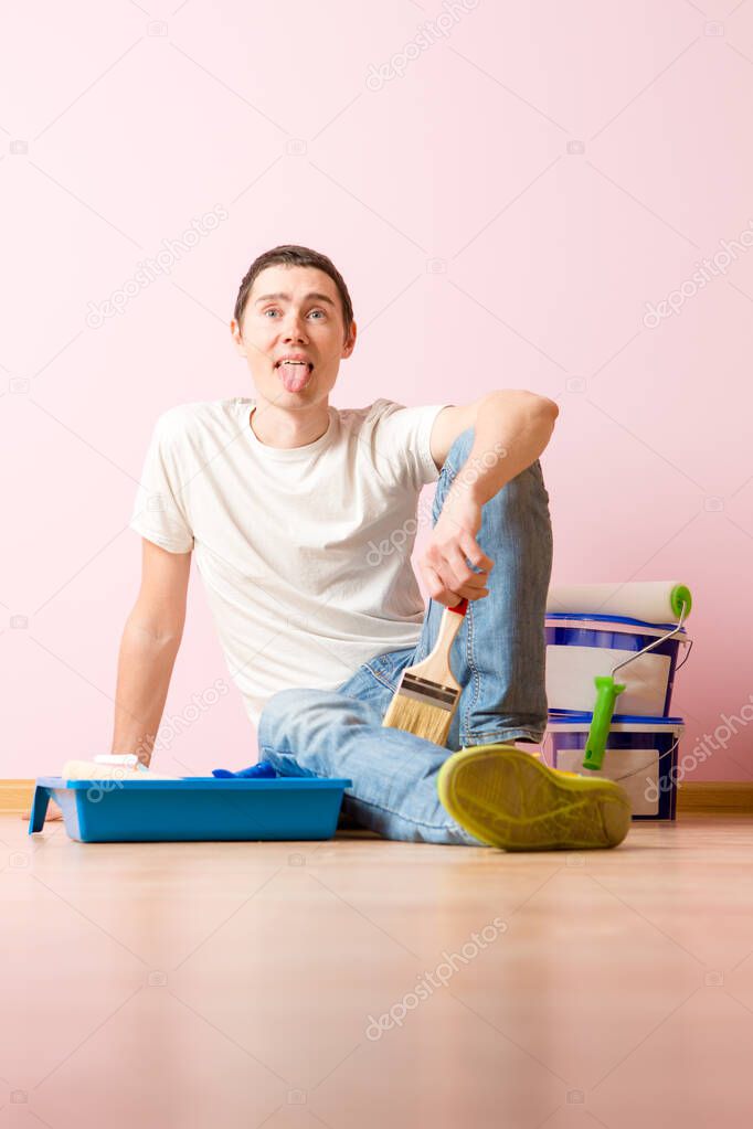 Photo of man with brush sitting on floor in new apartment