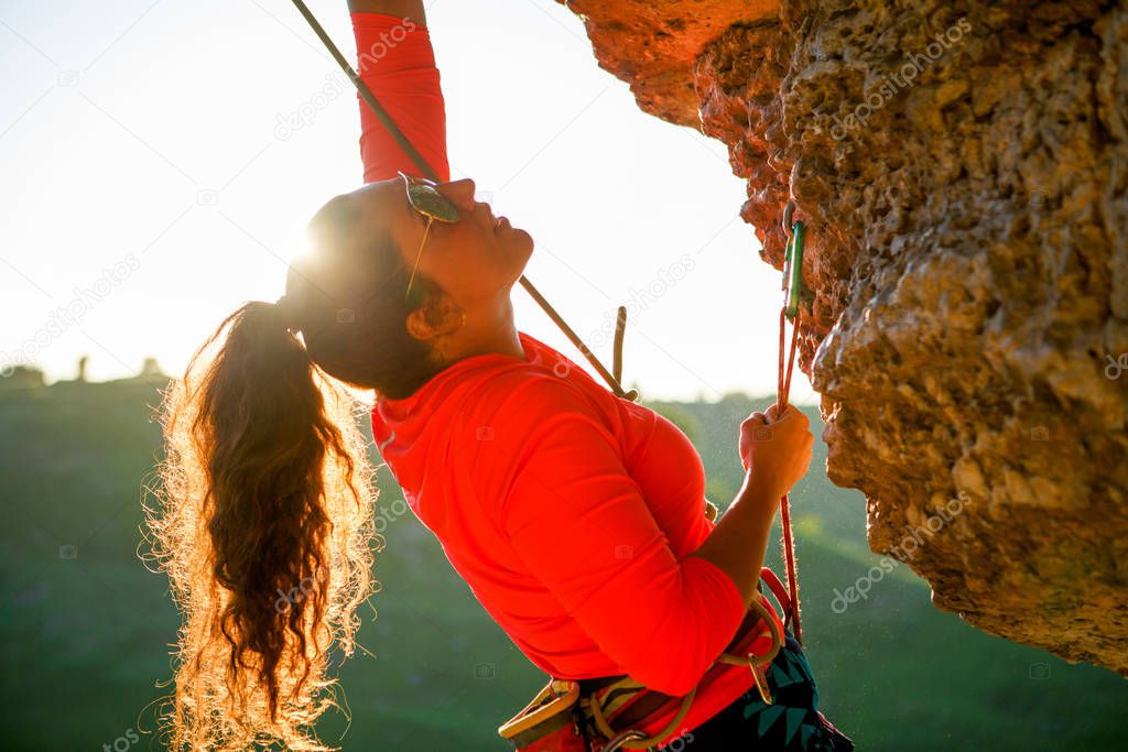 Photo of curly-haired female tourist clambering over rock on summer day