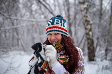 Kış ormanlarında örgü şapkalı ve eşarplı gülümseyen esmer fotoğraf, çözülmüş arka plan.
