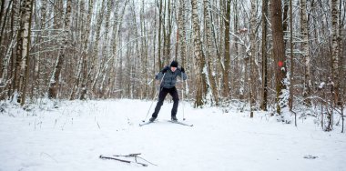 Kışın ormanda gri ceketli bir erkek kayakçının fotoğrafı.
