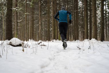 Spor giyimli bir adamın görüntüsü, kış ormanlarında koşan kırmızı şapkalı.